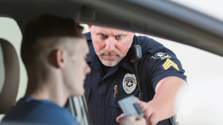 a police officer reaches into the car window as the young driver hands over his license