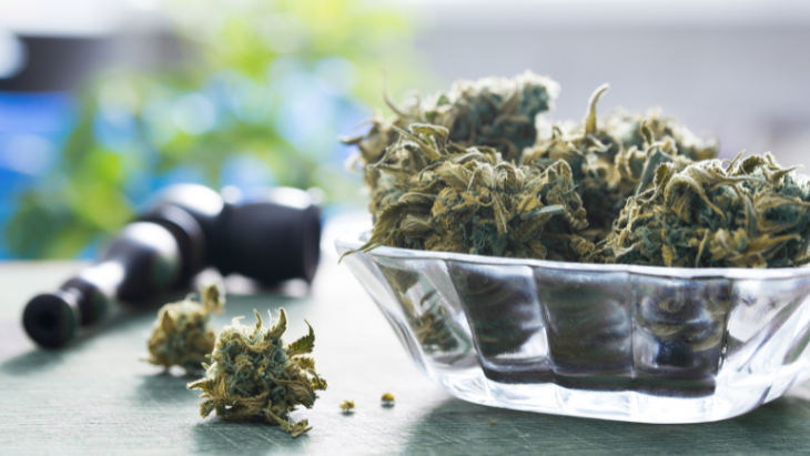 a glass bowl of legal cannabis flower sits on a table next a pipe